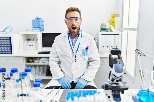 Middle age man working at scientist laboratory scared and amazed with open mouth for surprise, disbelief face