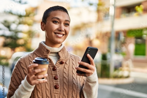 Young hispanic woman with short hair smiling happy drinking a cup of coffee and using smartphone