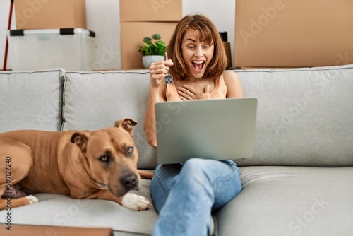 Young caucasian woman having video call and holding key sitting on sofa with dog at home
