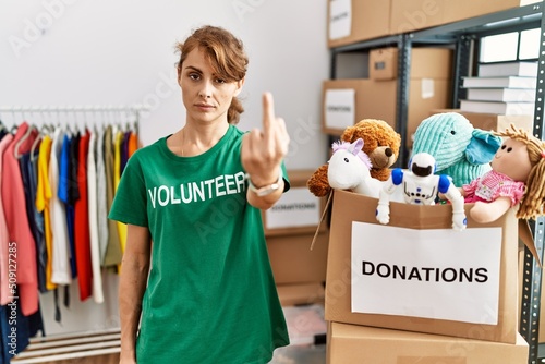 Beautiful caucasian woman wearing volunteer t shirt at donations stand showing middle finger, impolite and rude fuck off expression