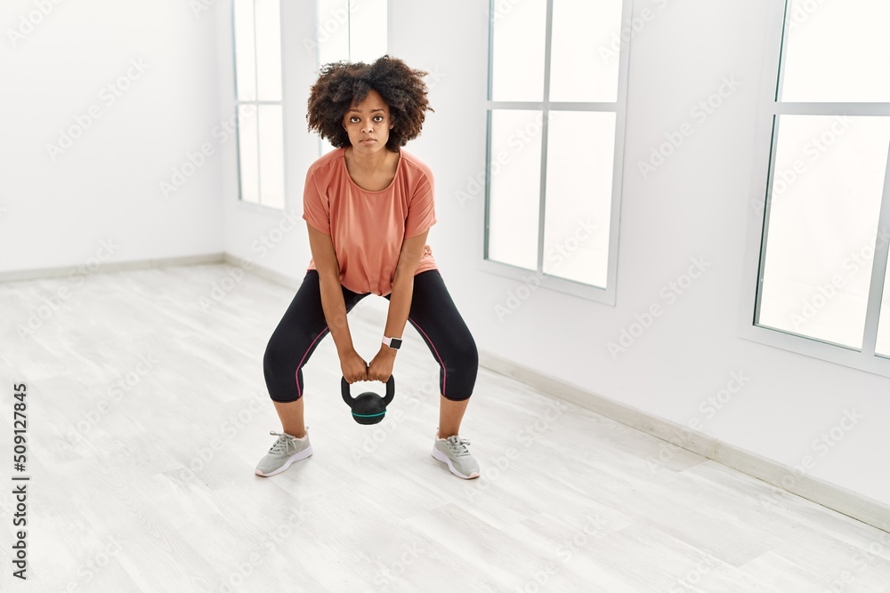 Young african american woman training using kettlebell at sport center