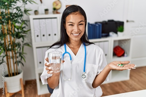 Young latin woman wearing doctor uniform holding pills at clinic