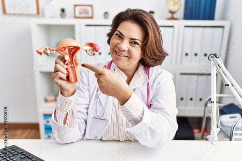 Middle age hispanic woman wearing doctor uniform holding uterus at clinic