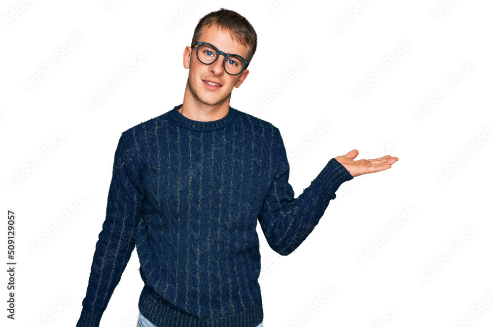 Young blond man wearing casual clothes and glasses smiling cheerful presenting and pointing with palm of hand looking at the camera. Young blond man wearing casual clothes and glasses smiling cheerful presenting and pointing with palm of hand looking at the camera.