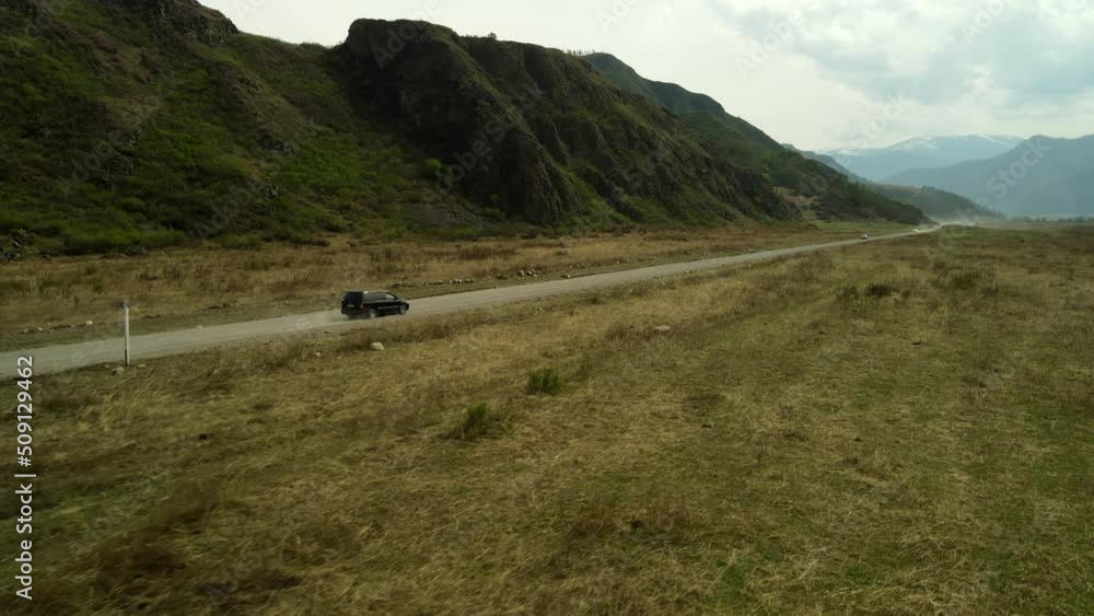 The SUV is moving along an unpaved road against the backdrop of mountain peisaage. Aerial photography of a car trip. The SUV is moving along an unpaved road against the backdrop of mountain peisaage. Aerial photography of a car trip.