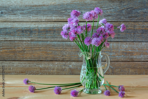 Bouquet of purple flowers of decorative onions in a glass vase on a wooden background