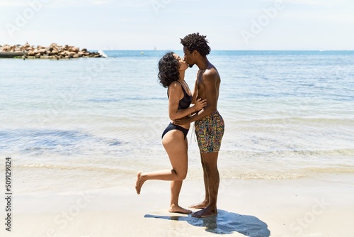Young interracial tourist couple wearing swimwear kissing and hugging at the beach.