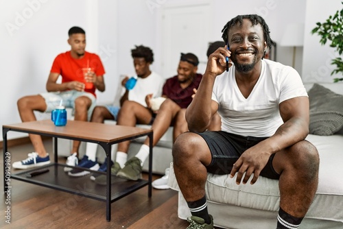 Group of african american people sitting on the sofa at home. Man smiling happy talking on the smartphone.