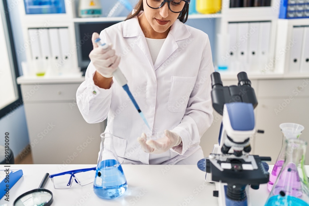 Young hispanic woman wearing scientist uniform using pipette working at laboratory Young hispanic woman wearing scientist uniform using pipette working at laboratory