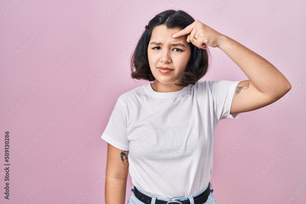 Young hispanic woman wearing casual white t shirt over pink background pointing unhappy to pimple on forehead, ugly infection of blackhead. acne and skin problem Young hispanic woman wearing casual white t shirt over pink background pointing unhappy to pimple on forehead, ugly infection of blackhead. acne and skin problem