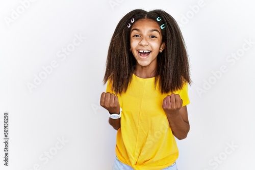 Young african american girl standing over white isolated background celebrating surprised and amazed for success with arms raised and open eyes. winner concept.