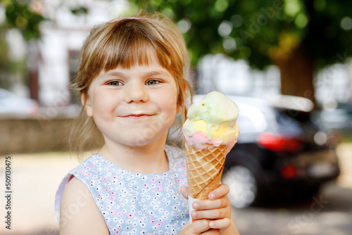 Little preschool girl eating ice cream in waffle cone on sunny summer day. Happy toddler child eat icecream dessert. Sweet food on hot warm summertime days. Bright light  colorful ice-cream