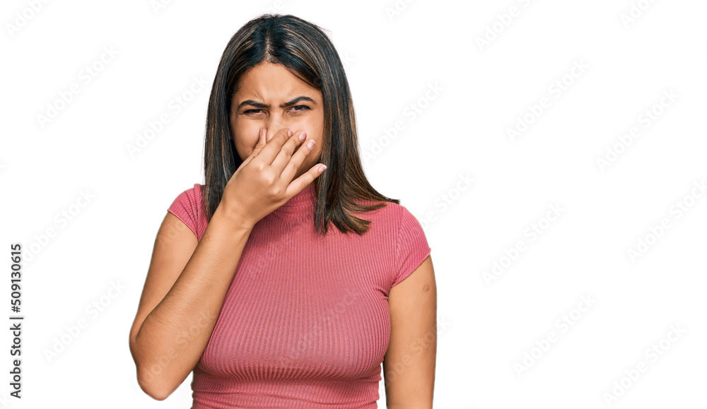Young hispanic girl wearing casual t shirt smelling something stinky and disgusting, intolerable smell, holding breath with fingers on nose. bad smell Young hispanic girl wearing casual t shirt smelling something stinky and disgusting, intolerable smell, holding breath with fingers on nose. bad smell