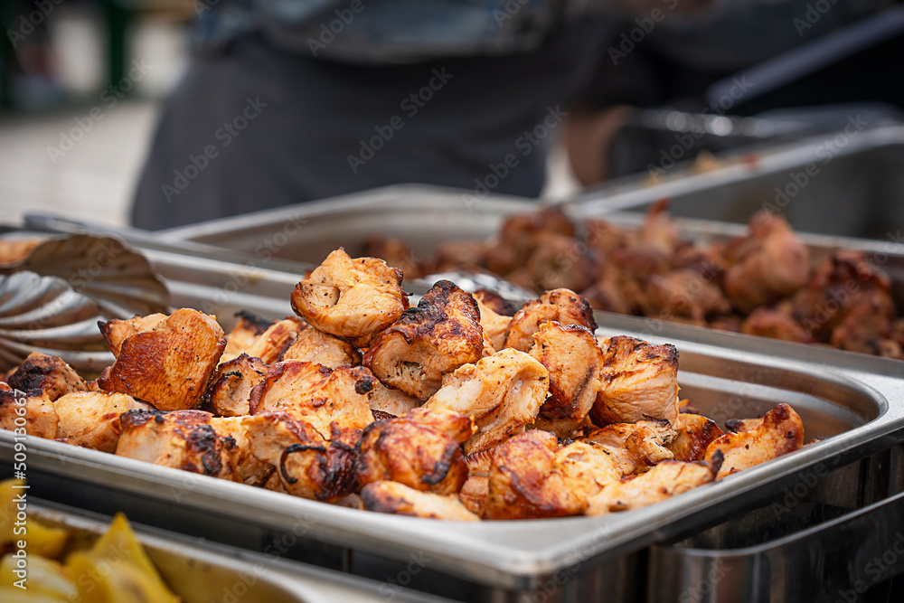 Bunch or pile of tasty juicy slabs of pork meat cooked, fried, grilled or roasted on outdoor restaurant kitchen barbeque grill on skewers laying in special metal container prepared for summer picnic