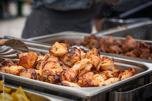Bunch or pile of tasty juicy slabs of pork meat cooked, fried, grilled or roasted on outdoor restaurant kitchen barbeque grill on skewers laying in special metal container prepared for summer picnic