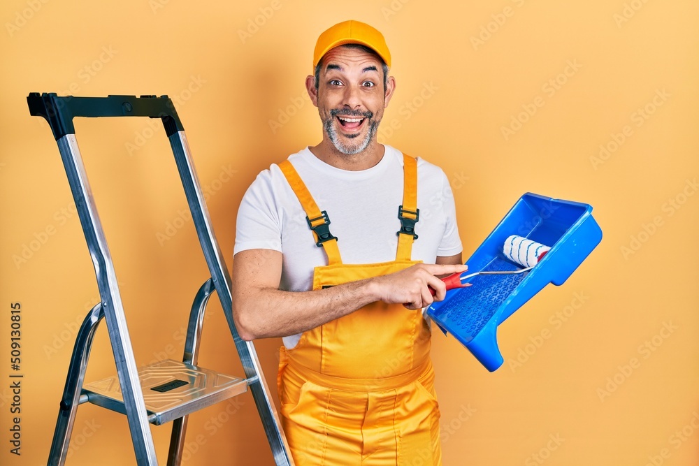 Handsome middle age man with grey hair holding roller painter celebrating crazy and amazed for success with open eyes screaming excited. Handsome middle age man with grey hair holding roller painter celebrating crazy and amazed for success with open eyes screaming excited.