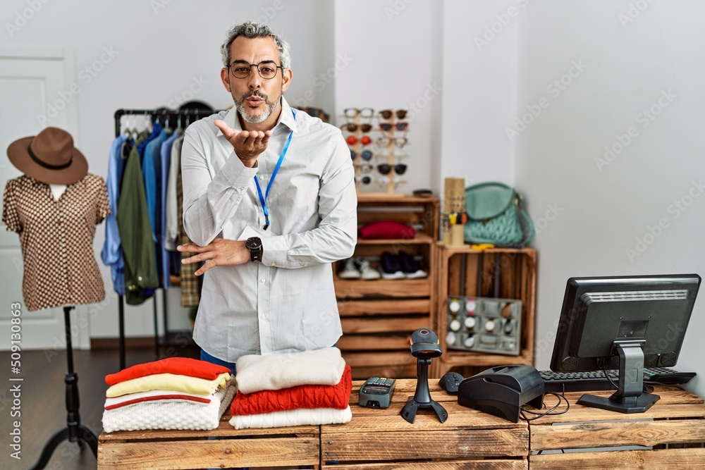 Middle age hispanic man working as manager at retail boutique looking at the camera blowing a kiss with hand on air being lovely and sexy. love expression. Middle age hispanic man working as manager at retail boutique looking at the camera blowing a kiss with hand on air being lovely and sexy. love expression.