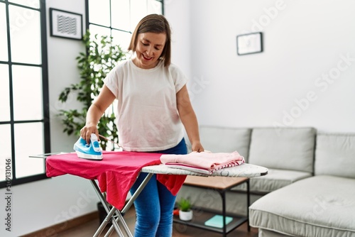 Middle age hispanic woman ironing clothes at home