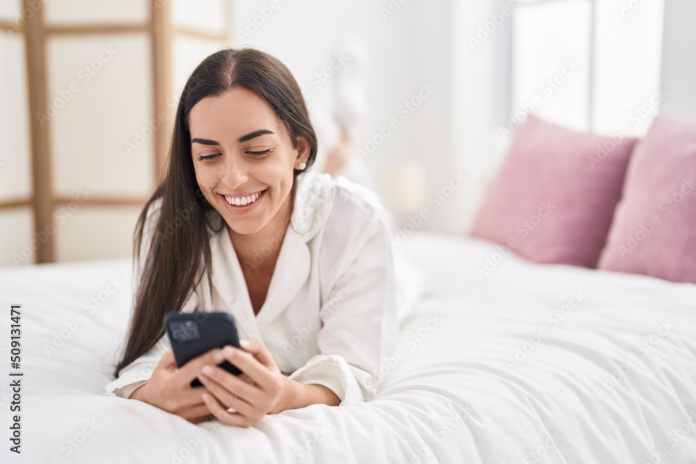 Young hispanic woman using smartphone lying on bed at bedroom Young hispanic woman using smartphone lying on bed at bedroom