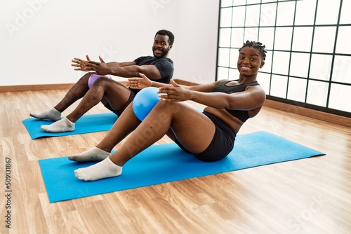 Young african american sporty couple smiling happy training pilates using ball at sport center.