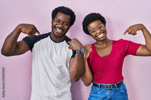 Young african american couple standing over pink background looking confident with smile on face  pointing oneself with fingers proud and happy.