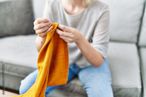 Young caucasian woman sewing using needle and thread at home