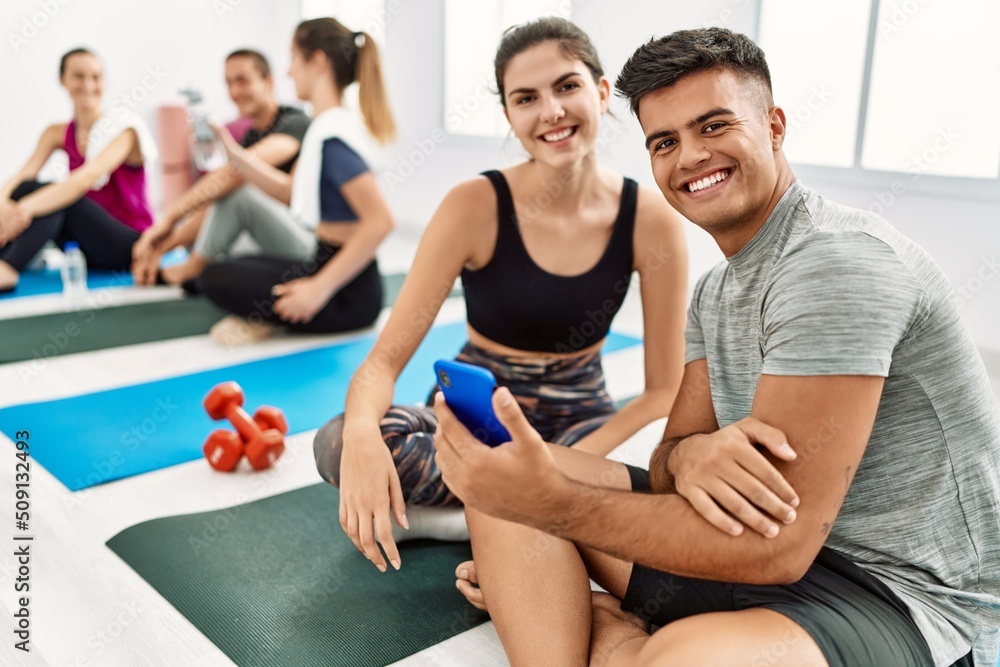 Fototapeta premium Group of young hispanic people smiling happy relaxing and using smartphone at sport center.