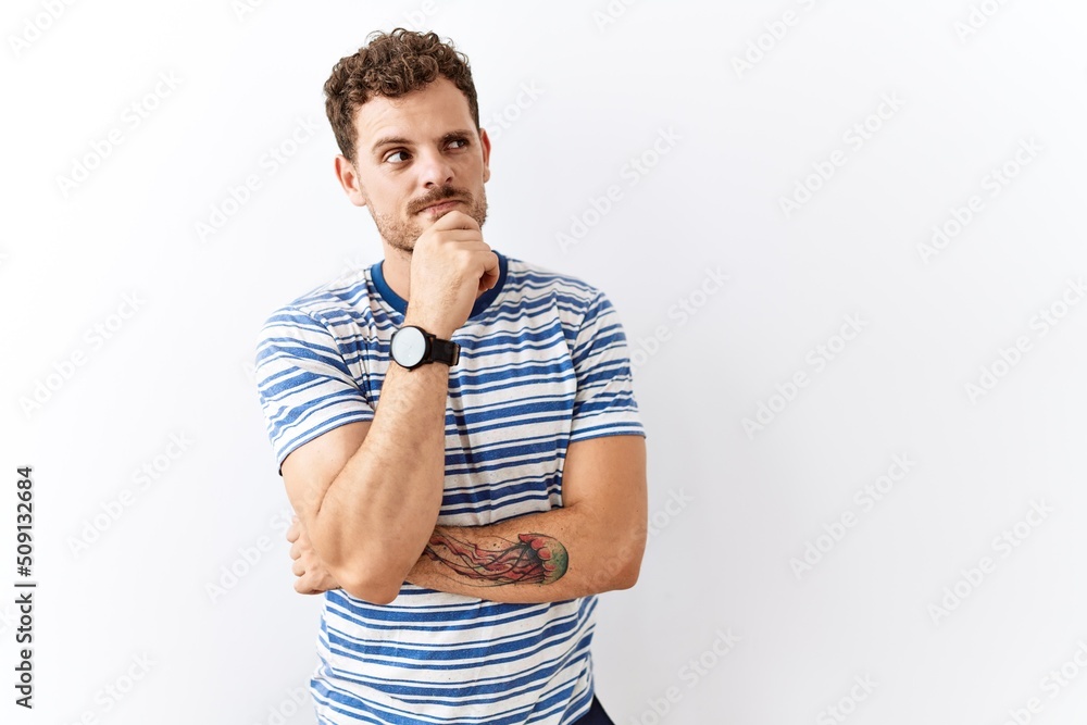 Handsome young man standing over isolated background with hand on chin thinking about question, pensive expression. smiling with thoughtful face. doubt concept. Handsome young man standing over isolated background with hand on chin thinking about question, pensive expression. smiling with thoughtful face. doubt concept.