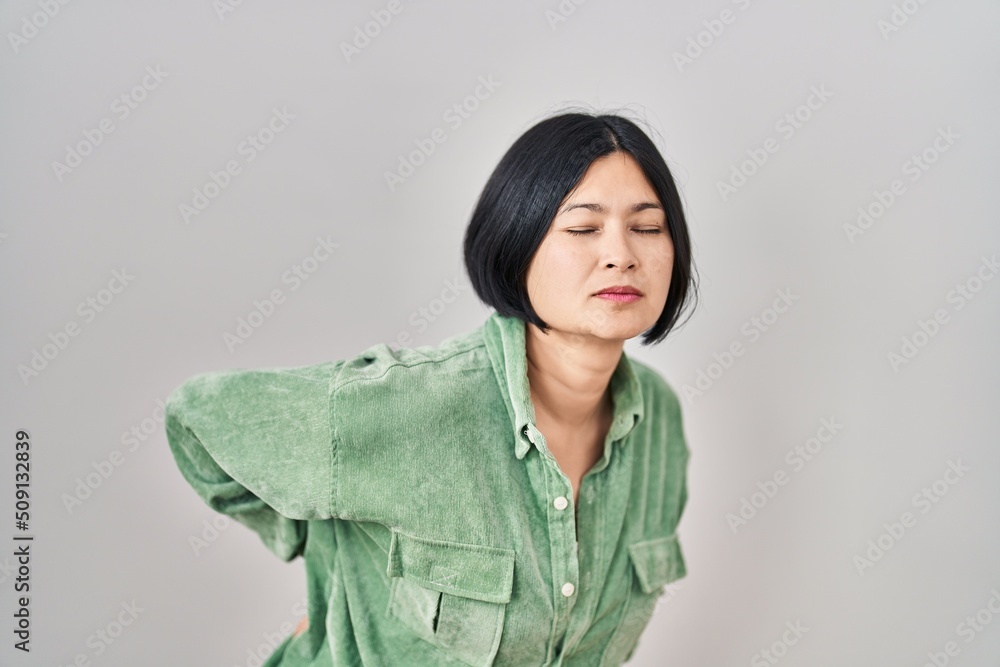 Young asian woman standing over white background suffering of backache, touching back with hand, muscular pain