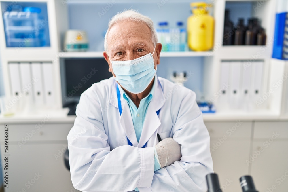 Senior man wearing scientist uniform and medical mask with arms crossed gesture at laboratory Senior man wearing scientist uniform and medical mask with arms crossed gesture at laboratory