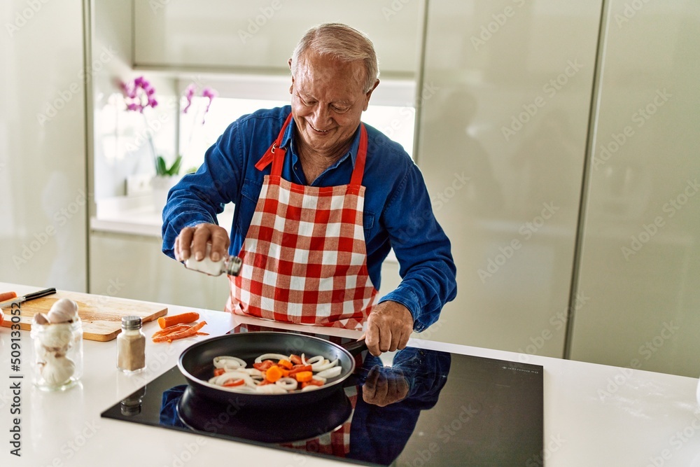 Senior man smiling confident pouring salt on frying pan at kitchen Senior man smiling confident pouring salt on frying pan at kitchen