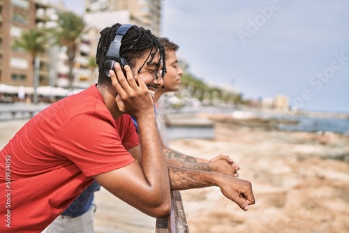 Two african american man smiling happy listening to music at the beach.