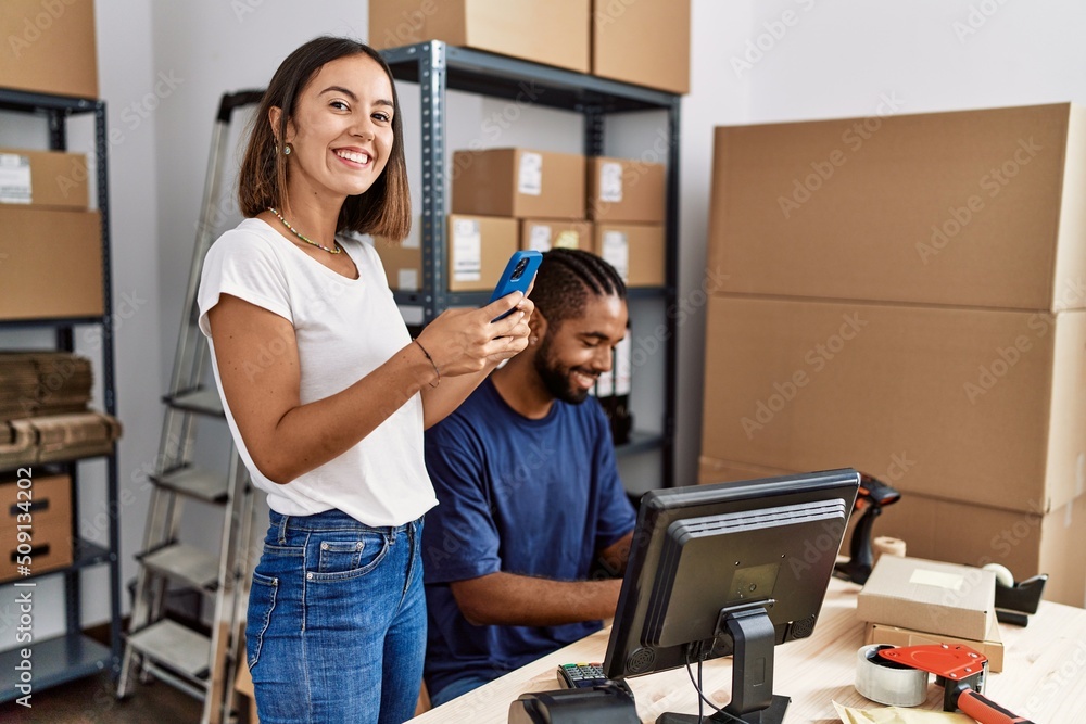 Man and woman business partners using smartphone and packing order at storehouse Man and woman business partners using smartphone and packing order at storehouse