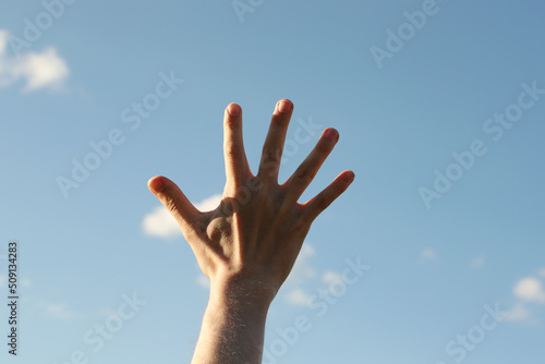 Young man right hand and blue sky. Photo was taken 22 May 2022 year, MSK time in Russia.