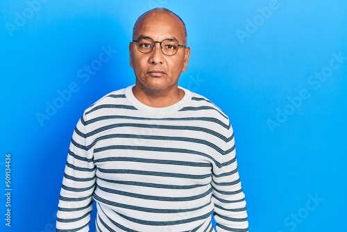 Middle age latin man wearing casual clothes and glasses relaxed with serious expression on face. simple and natural looking at the camera.