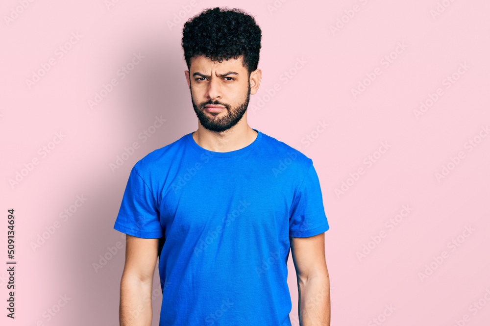 Young arab man with beard wearing casual blue t shirt relaxed with serious expression on face. simple and natural looking at the camera. Young arab man with beard wearing casual blue t shirt relaxed with serious expression on face. simple and natural looking at the camera.