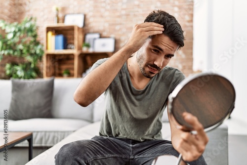 Young hispanic man lookin hair on mirror at home photo