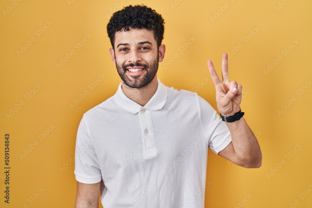 Arab man standing over yellow background showing and pointing up with fingers number two while smiling confident and happy. Arab man standing over yellow background showing and pointing up with fingers number two while smiling confident and happy.