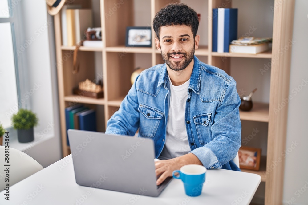 Young arab man using laptop drinking coffe sitting on table at home Young arab man using laptop drinking coffe sitting on table at home