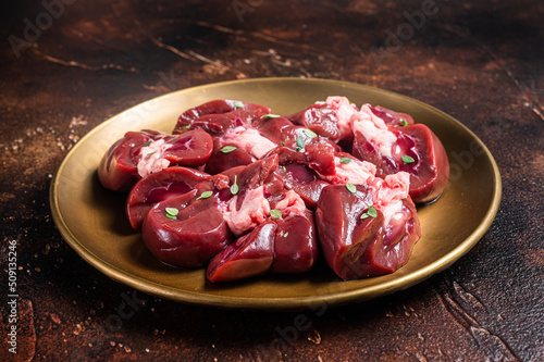 Raw Beef kidney, fresh sliced offal meat on plate. Dark background. Top view