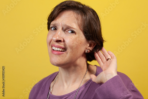 Attractive mature woman in purple blouse on a yellow background can't hear. Difficulty hearing concept image. photo