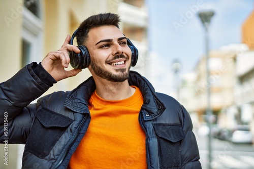 Handsome hispanic man with beard smiling happy and confident at the city wearing winter coat