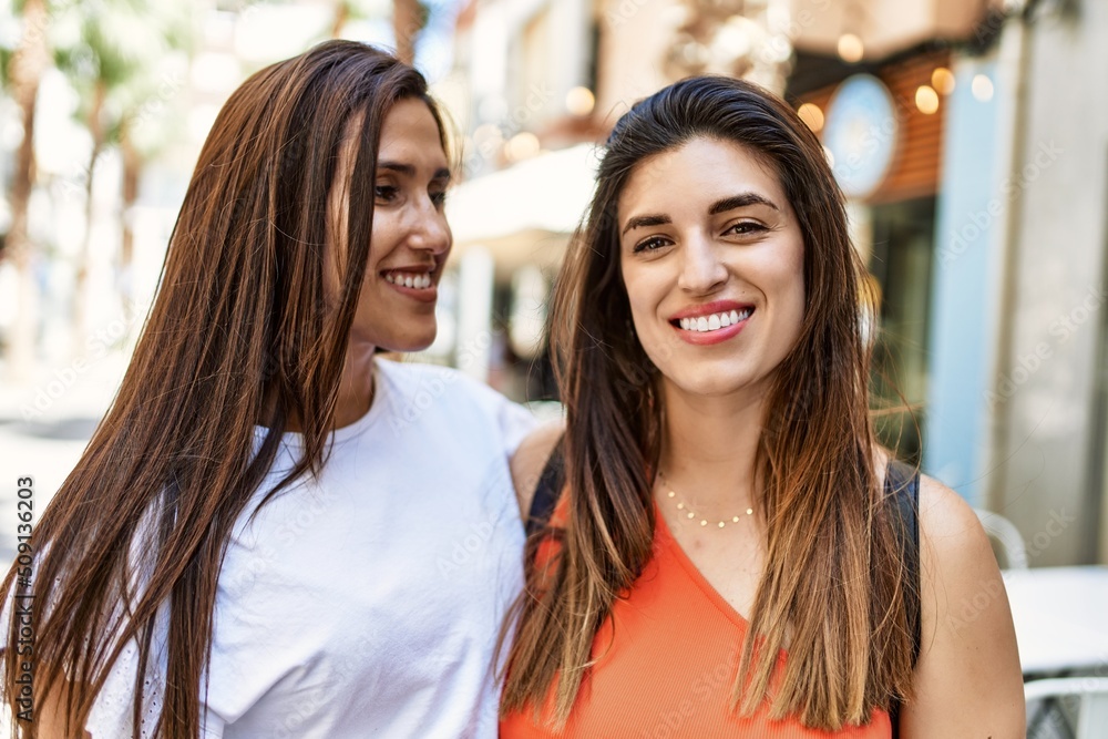 Two latin girls smiling happy and hugging at the city.