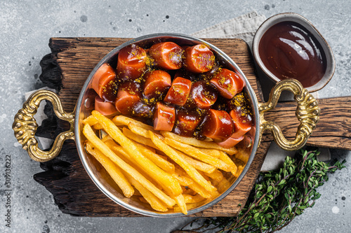 Traditional German currywurst sausage, served with chips or French fries in a pan. Gray background. Top view
