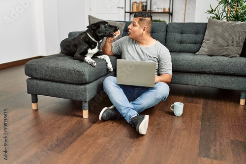 Young hispanic man using laptop sitting on the floor with dog at home. © Krakenimages.com