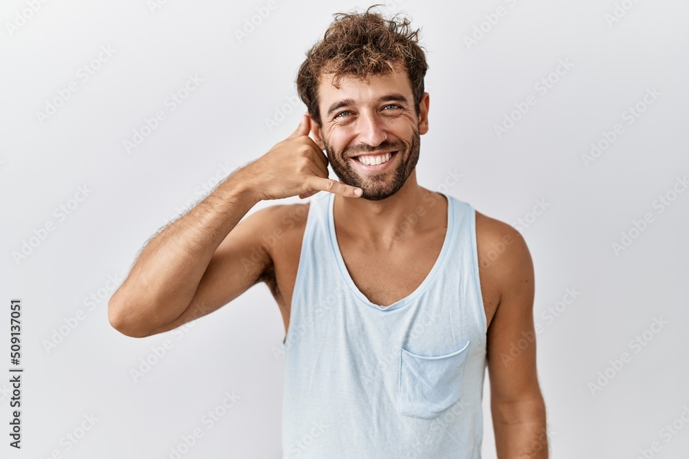 Young handsome man standing over isolated background smiling doing phone gesture with hand and fingers like talking on the telephone. communicating concepts. Young handsome man standing over isolated background smiling doing phone gesture with hand and fingers like talking on the telephone. communicating concepts.