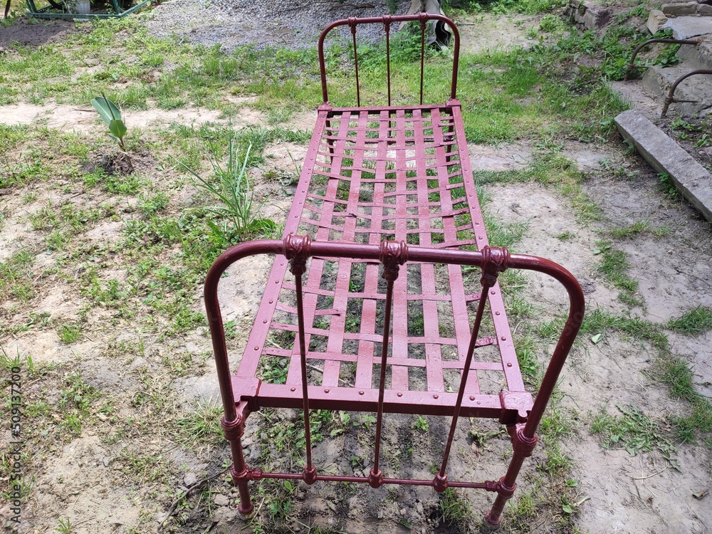 a very old cherry-coloured iron bed stands on the ground in the yard a very old cherry-coloured iron bed stands on the ground in the yard