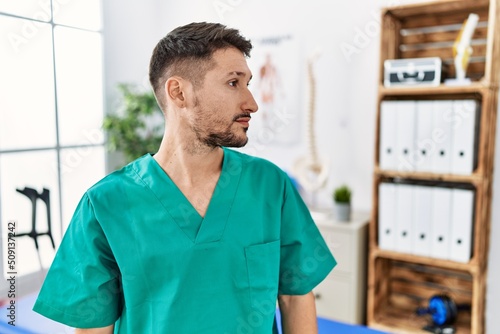 Young physiotherapist man working at pain recovery clinic looking to side, relax profile pose with natural face and confident smile.