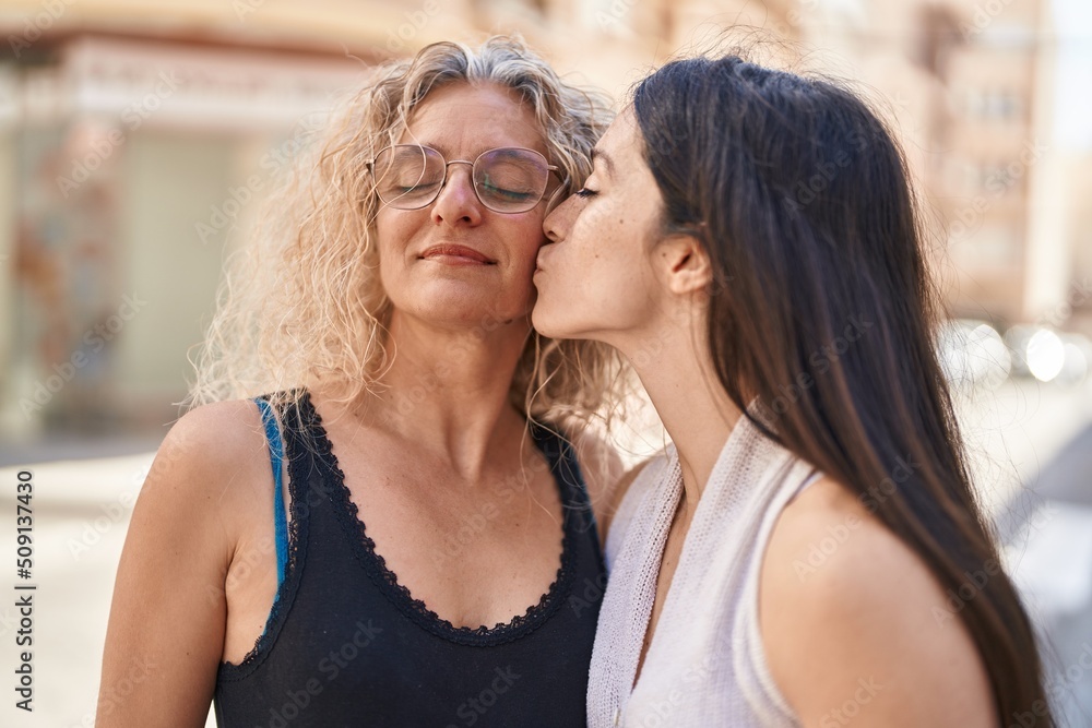 Two women mother and daughter standing together kissing at street