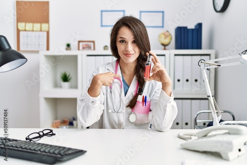 Young doctor woman holding electronic cigarette at medical clinic pointing finger to one self smiling happy and proud